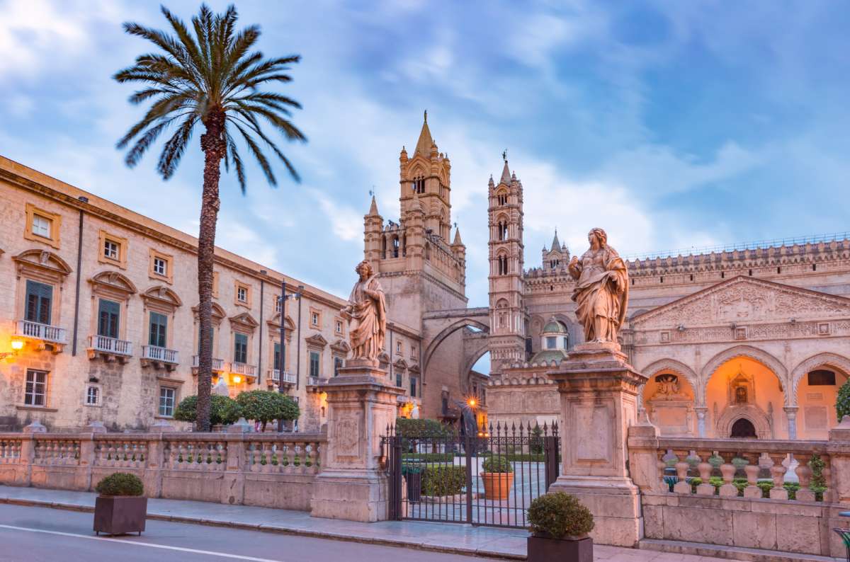 a photo of the Arab-Norman facade of Palermo Cathedral with its towers, statues and a palm tree, Palermo, Sicily, Italy