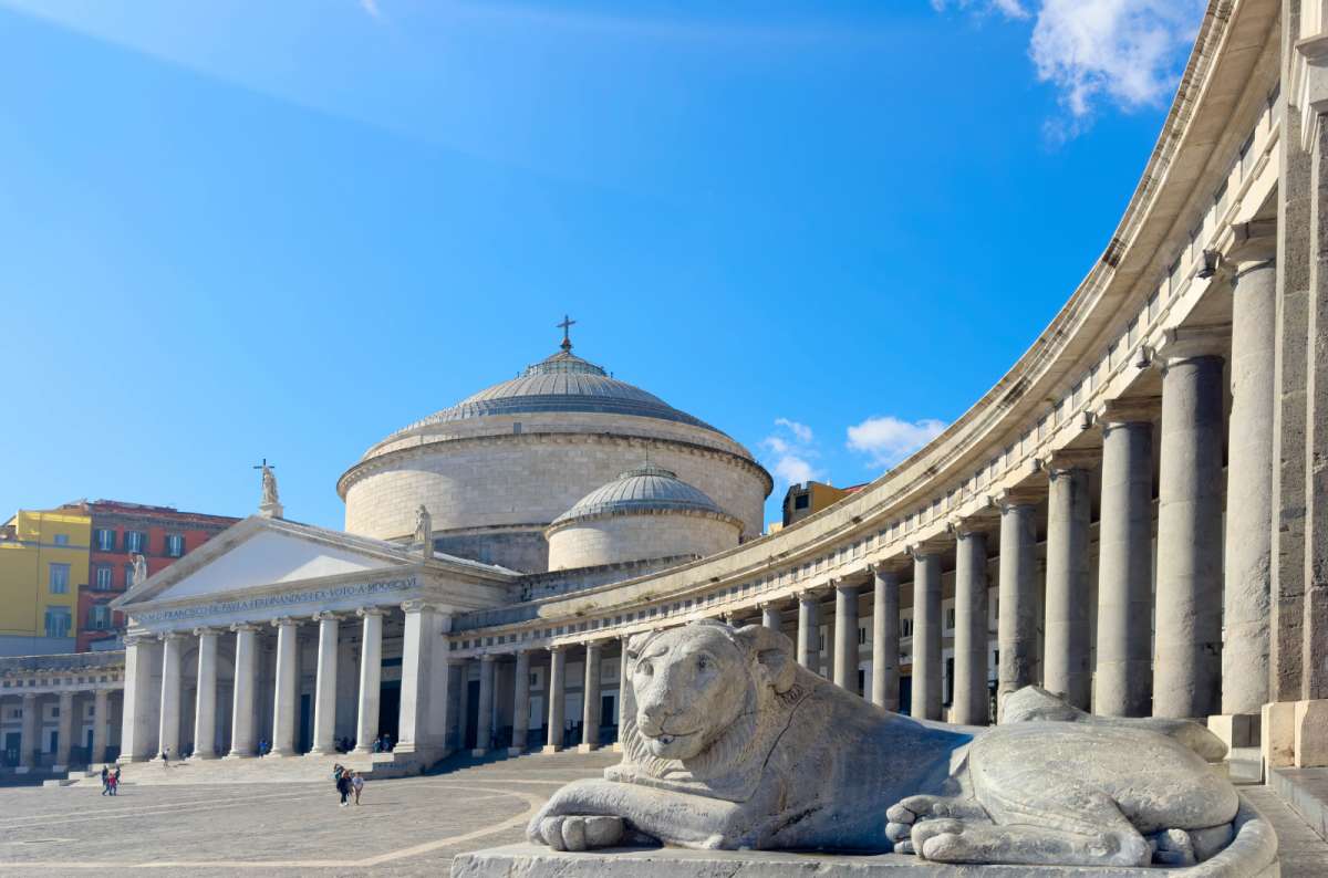 a photo of the Basilica of San Francesco di Paola and its curved colonnade on Piazza del Plebiscito with a stone lion statue in front, Naples, Italy