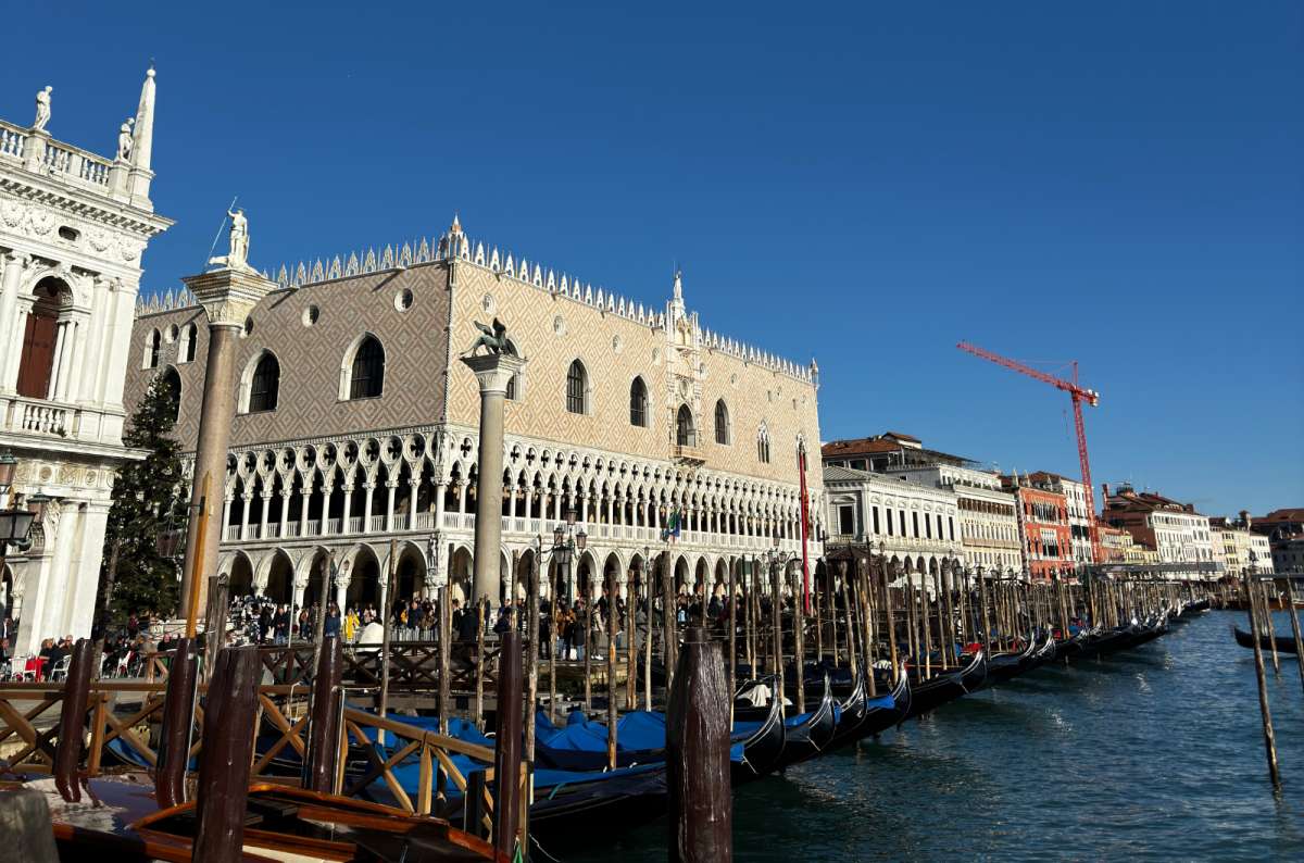 a photo of the Doge's Palace and moored gondolas on the waterfront under a clear blue sky, Venice, Italy, photo by Next Level of Travel
