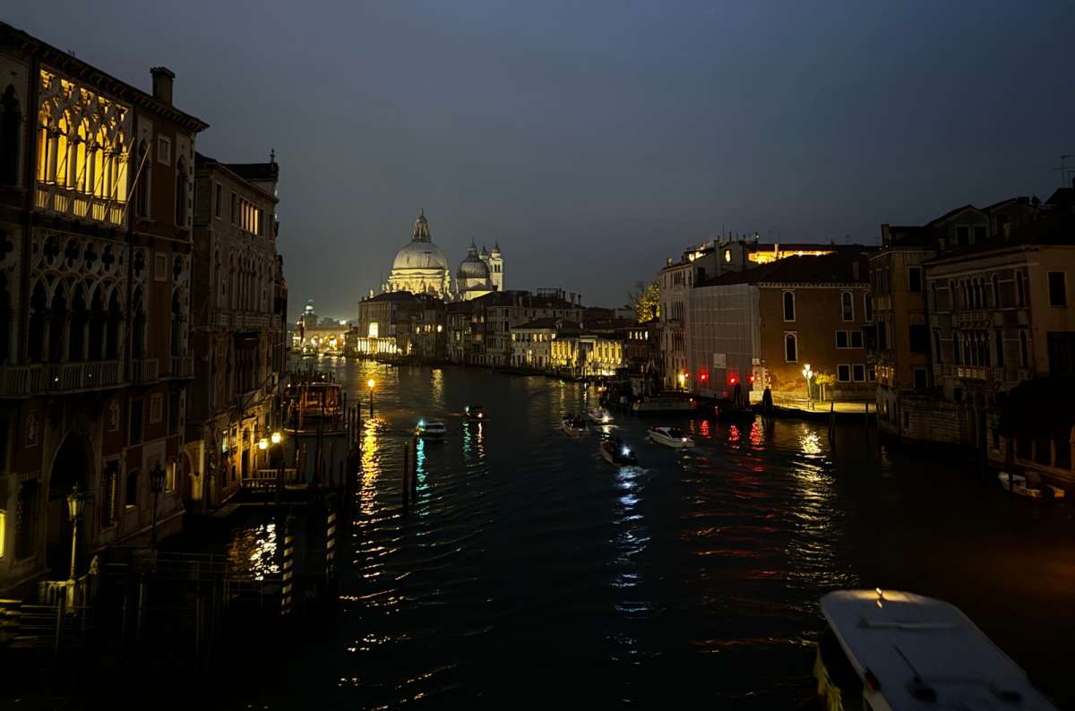 a photo of the Grand Canal at night with lit palazzos and the dome of Santa Maria della Salute in the distance, Venice, Italy, photo by Next Level of Travel