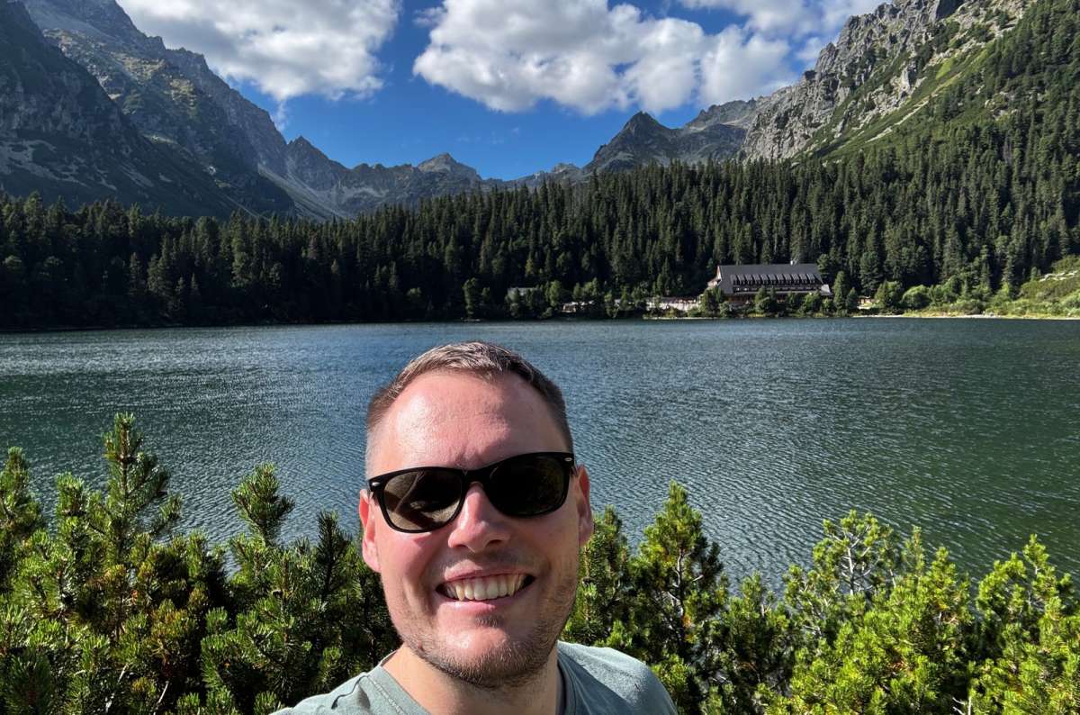 a photo of a tourist taking a selfie at Popradské pleso with the mountain hotel and the High Tatras behind, Slovakia, photo by Next Level of Travel
