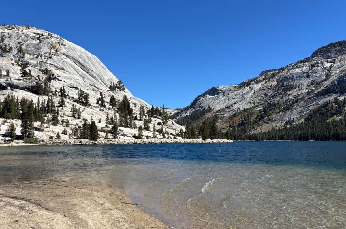 a photo of clear water on the sandy shore of Tenaya Lake below granite domes, Yosemite National Park, USA, photo by Next Level of Travel