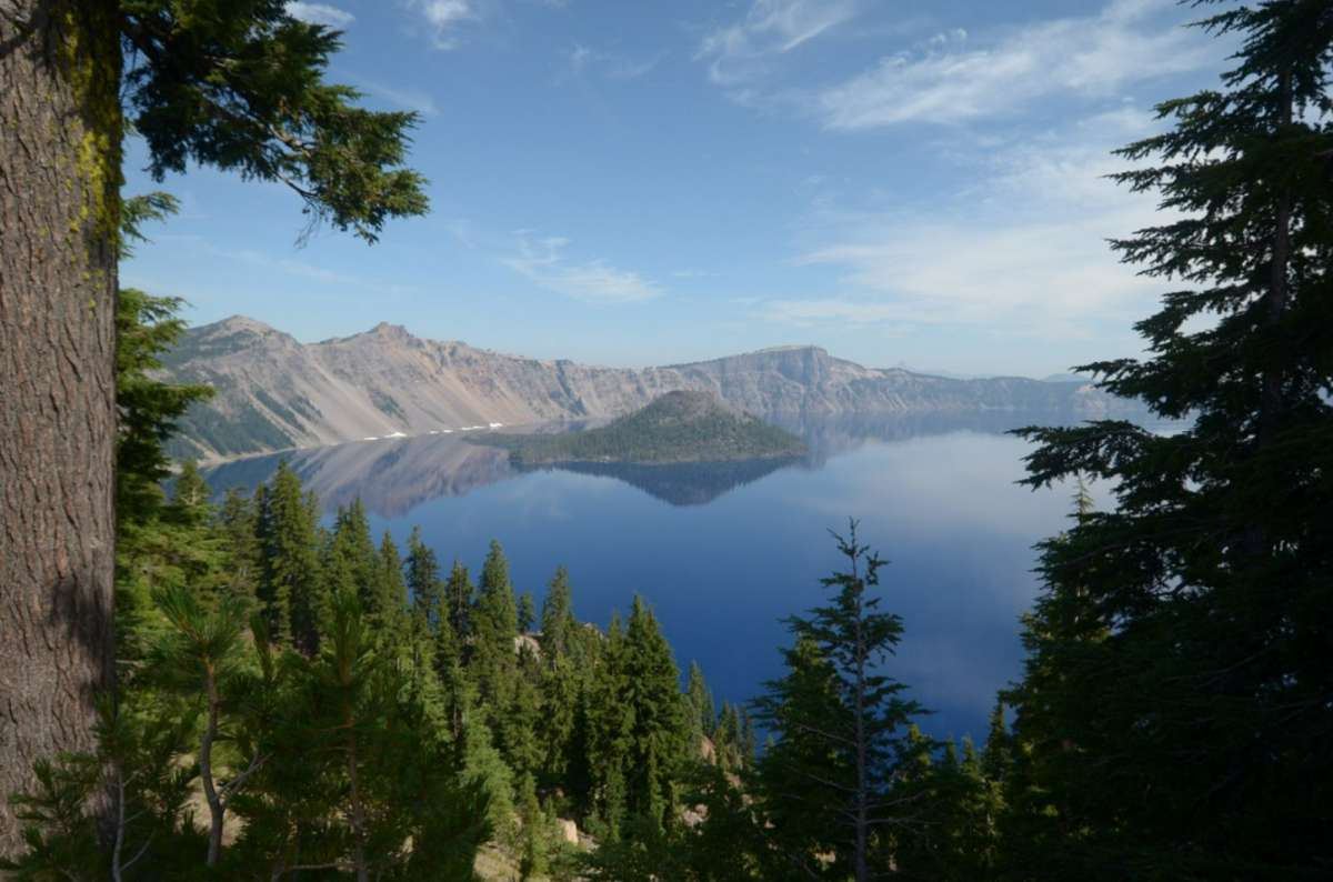 a photo of Crater Lake and Wizard Island seen through pine trees from the rim, Crater Lake National Park, Oregon, USA