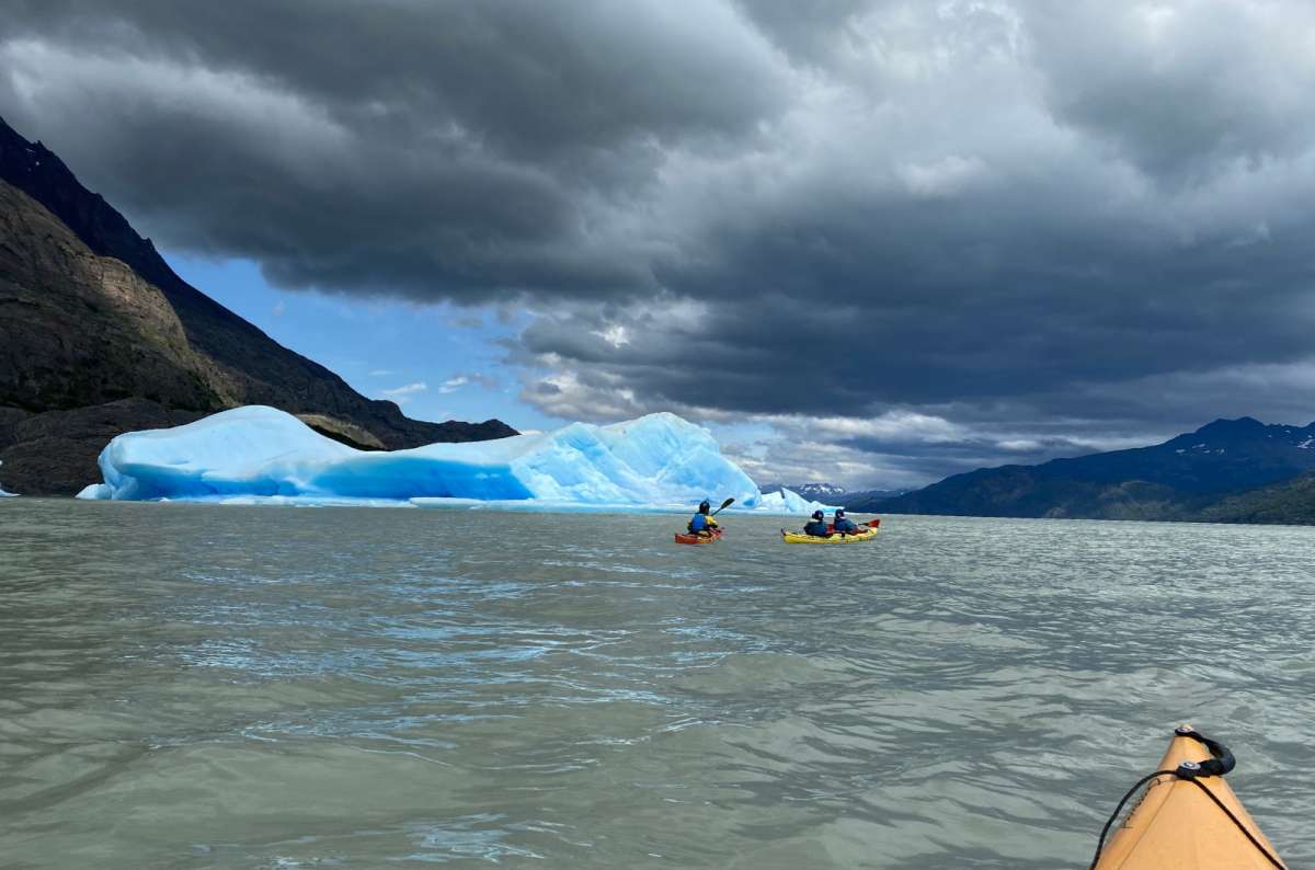 a photo of kayakers paddling past a blue iceberg on Lago Grey under storm clouds, Torres del Paine National Park, Chile, photo by Next Level of Travel