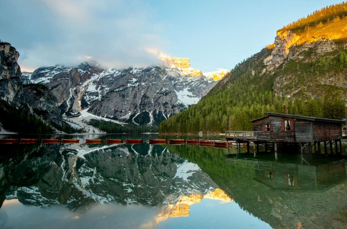 a photo of rowboats and the wooden boathouse at Lago di Braies with Croda del Becco reflected in the water, Dolomites, Italy