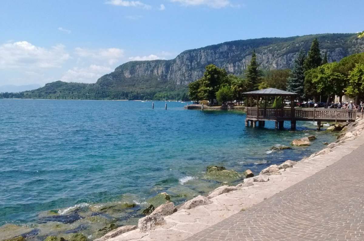 a photo of the lakeside promenade with a wooden pier and limestone cliffs on Lake Garda, Italy