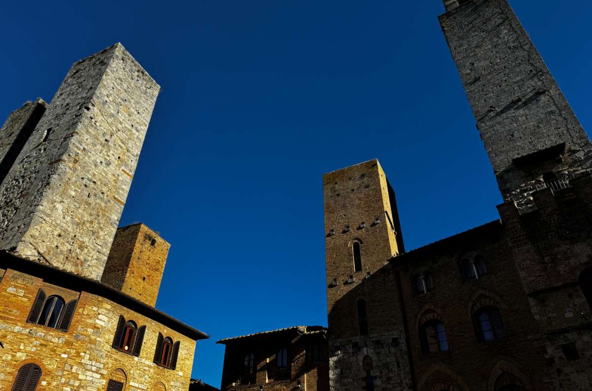 a photo looking up at the medieval stone towers of San Gimignano against a deep blue sky, San Gimignano, Italy, photo by Next Level of Travel