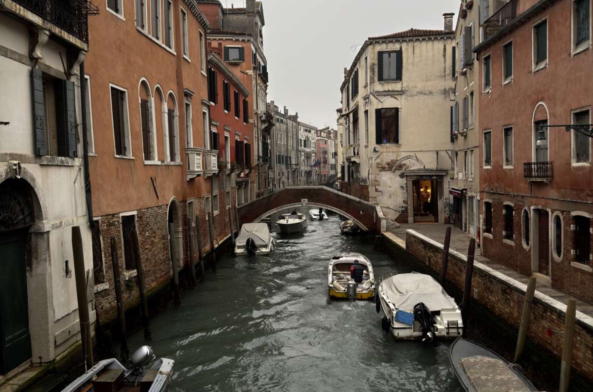 a photo of a quiet side canal lined with moored boats and old houses, Venice, Italy, photo by Next Level of Travel