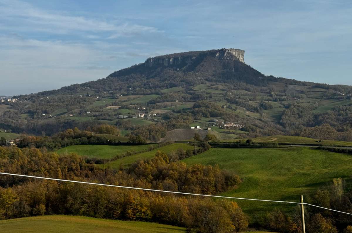 a photo of the flat-topped Rocca di Bismantova rising above green fields and autumn trees in the Apennine countryside, Emilia-Romagna, Italy, photo by Next Level of Travel