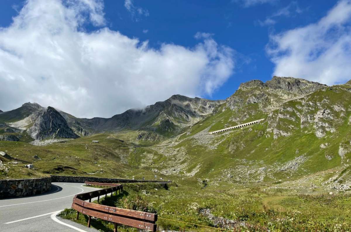 a photo of the winding road and green alpine valley on the Great Saint Bernard Pass, Aosta Valley, Italy, photo by Next Level of Travel