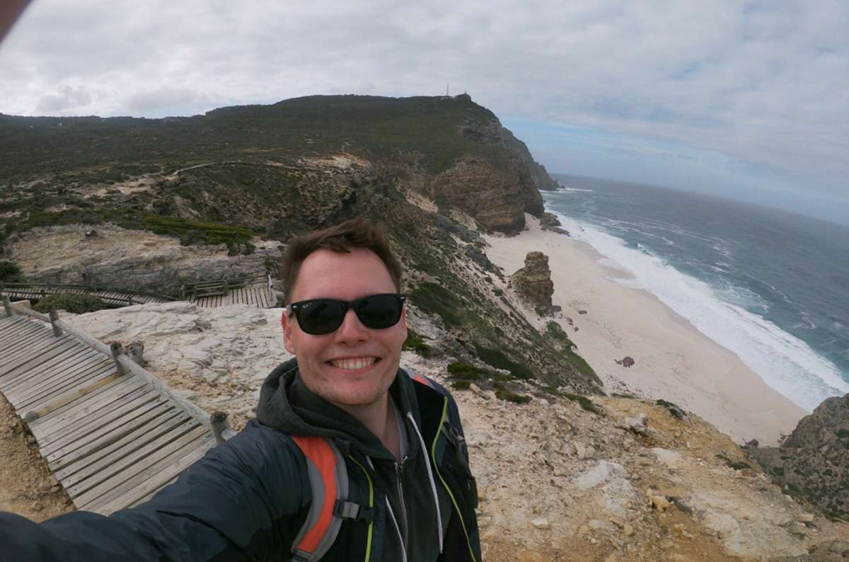 Tourist smiling into the camera on a beach trail in south africa on cloudy, windy day, photo by next level of travel