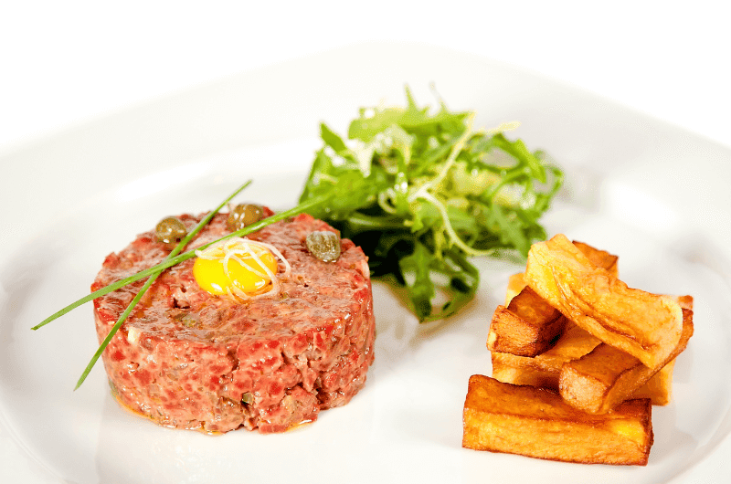 A plate of Belgian beef tartare served with a side of fries and a salad